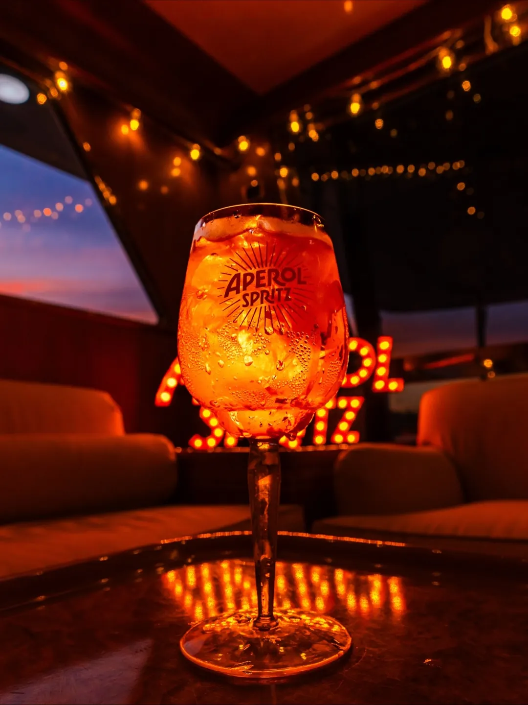 Aperol Spritz pe bar, între lumini ambientale calde, la un eveniment privat