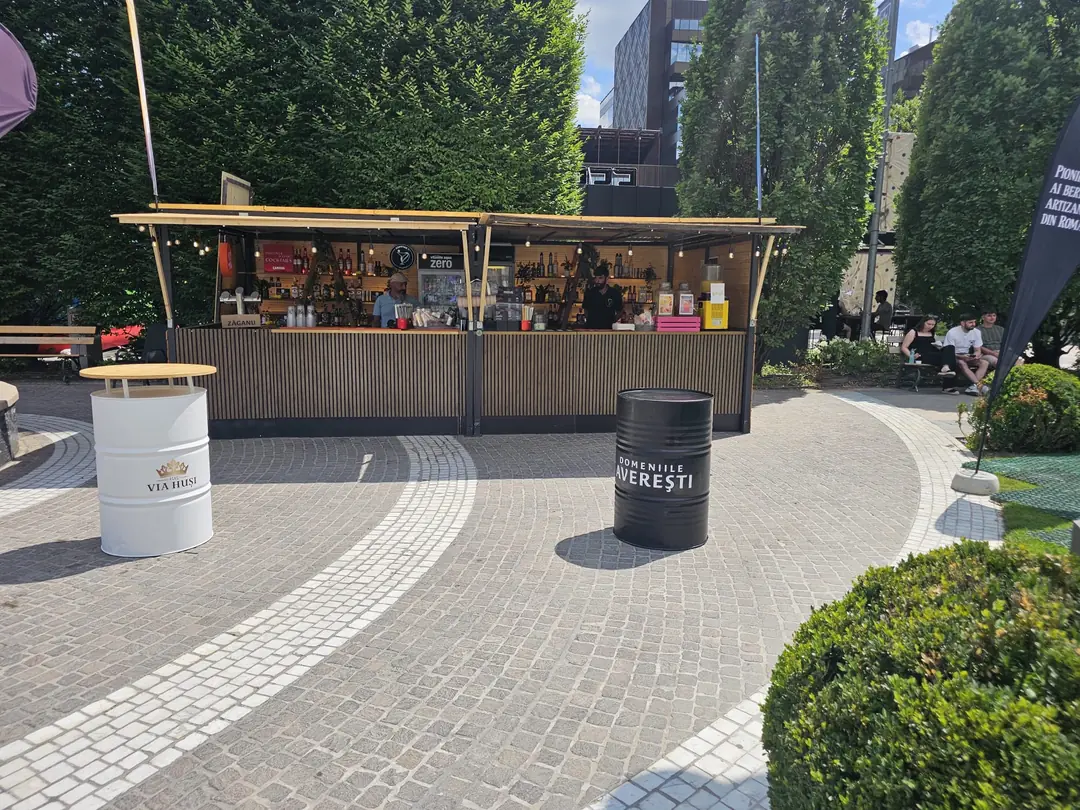 Bar mobil montat într-un parc urban pentru o activare de brand, cu butoaie branduite pe post de mese înalte