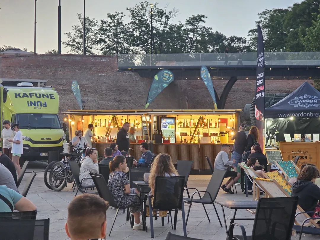 Bar mobil iluminat la un food fest, cu publicul așezat la mese în fața zidului de cărămidă al cetății