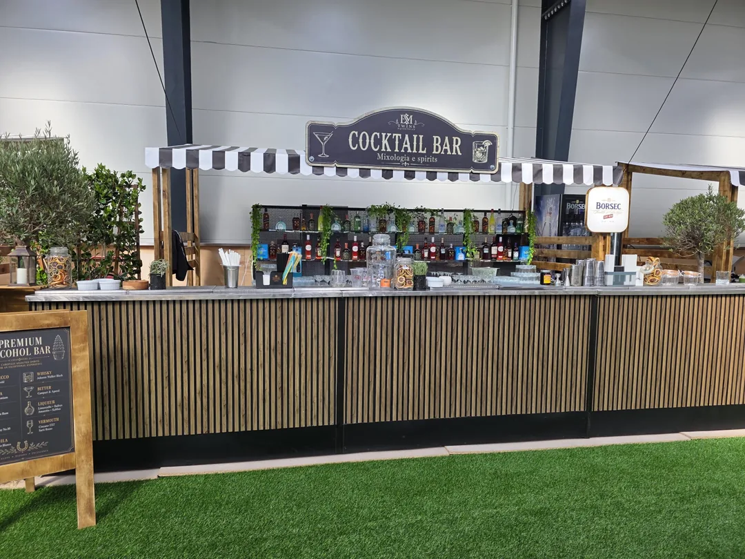Bar mobil modular văzut din față, cu backbar plin de sticle, plante agățătoare și blat de zinc