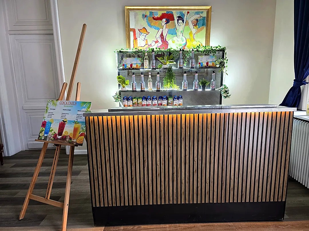 Bar de mocktailuri cu riflaje din lemn, raft de siropuri și meniu fără alcool, amenajat într-un salon elegant
