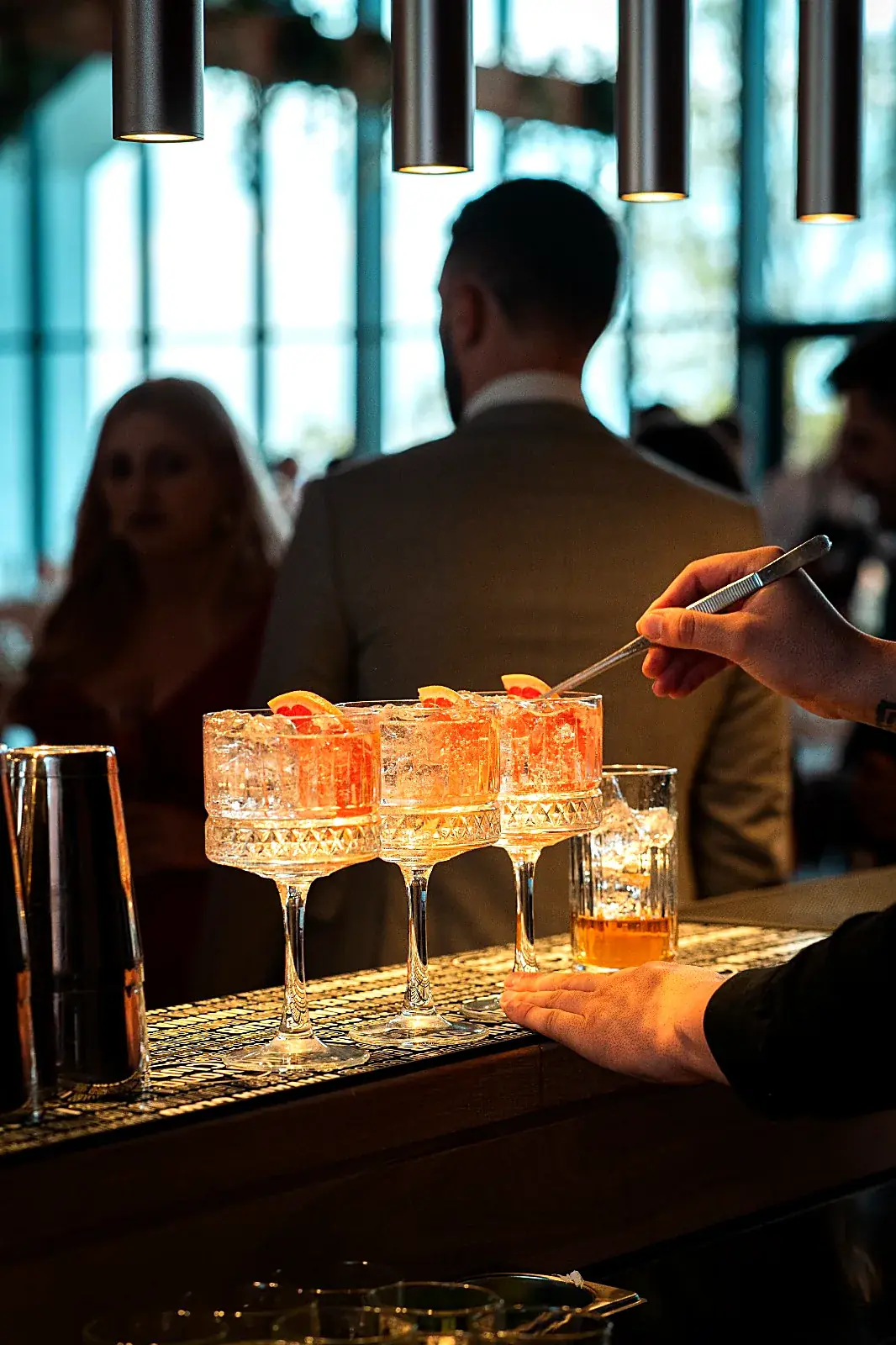 Barman garnisind cu grepfrut trei cocktailuri spritz în pahare coupe, la barul unui eveniment privat