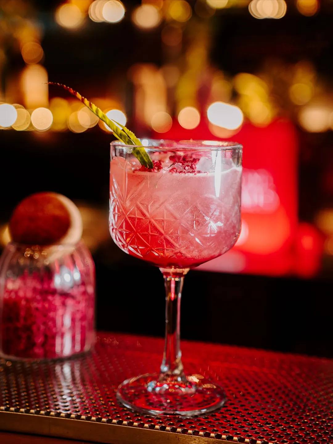 Cocktail signature servit într-un pahar de cristal, cu lumini calde de fundal