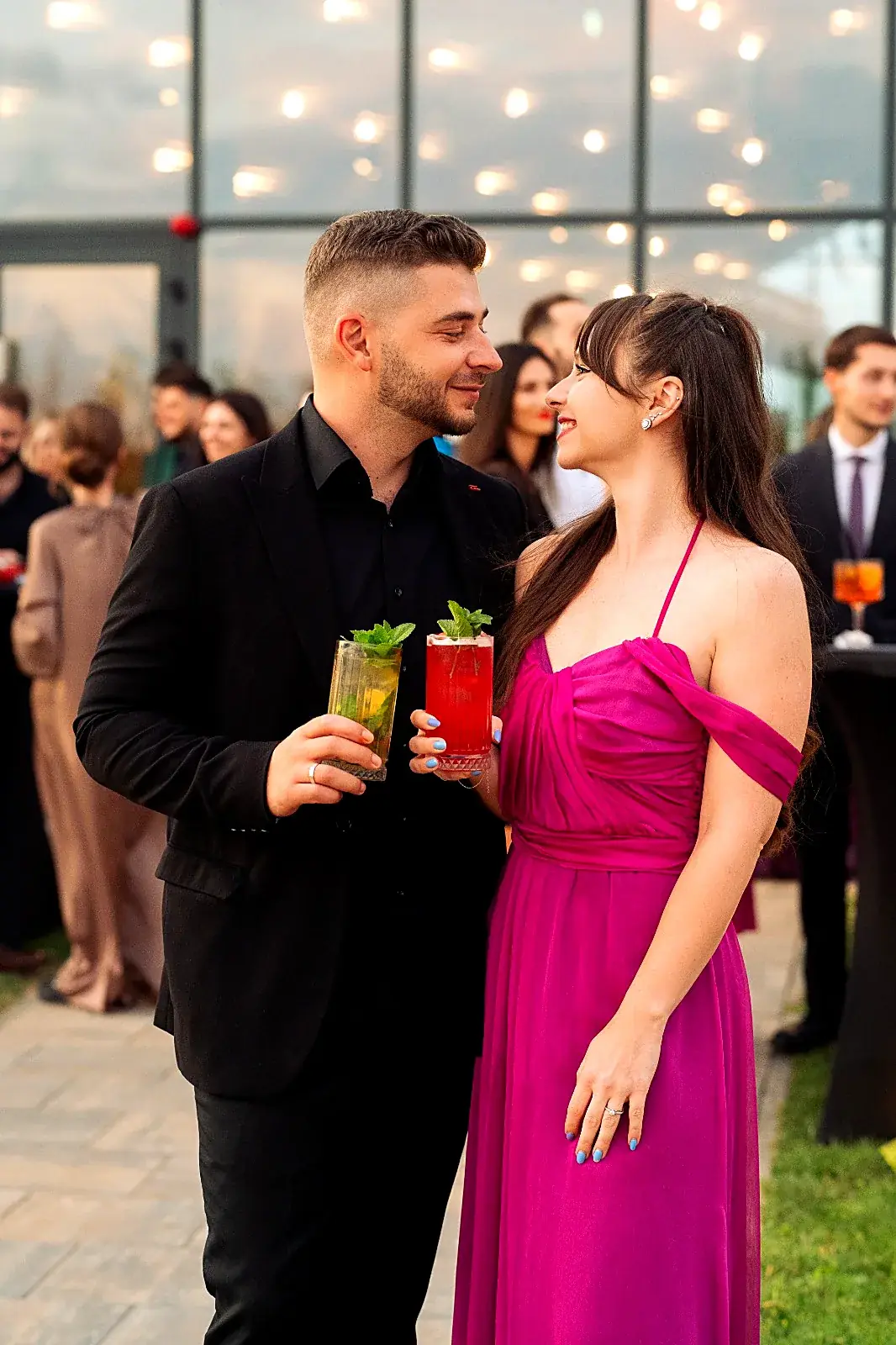 Cuplu elegant ținând în mână cocktailuri cu mentă, pe terasa unui eveniment privat la apus