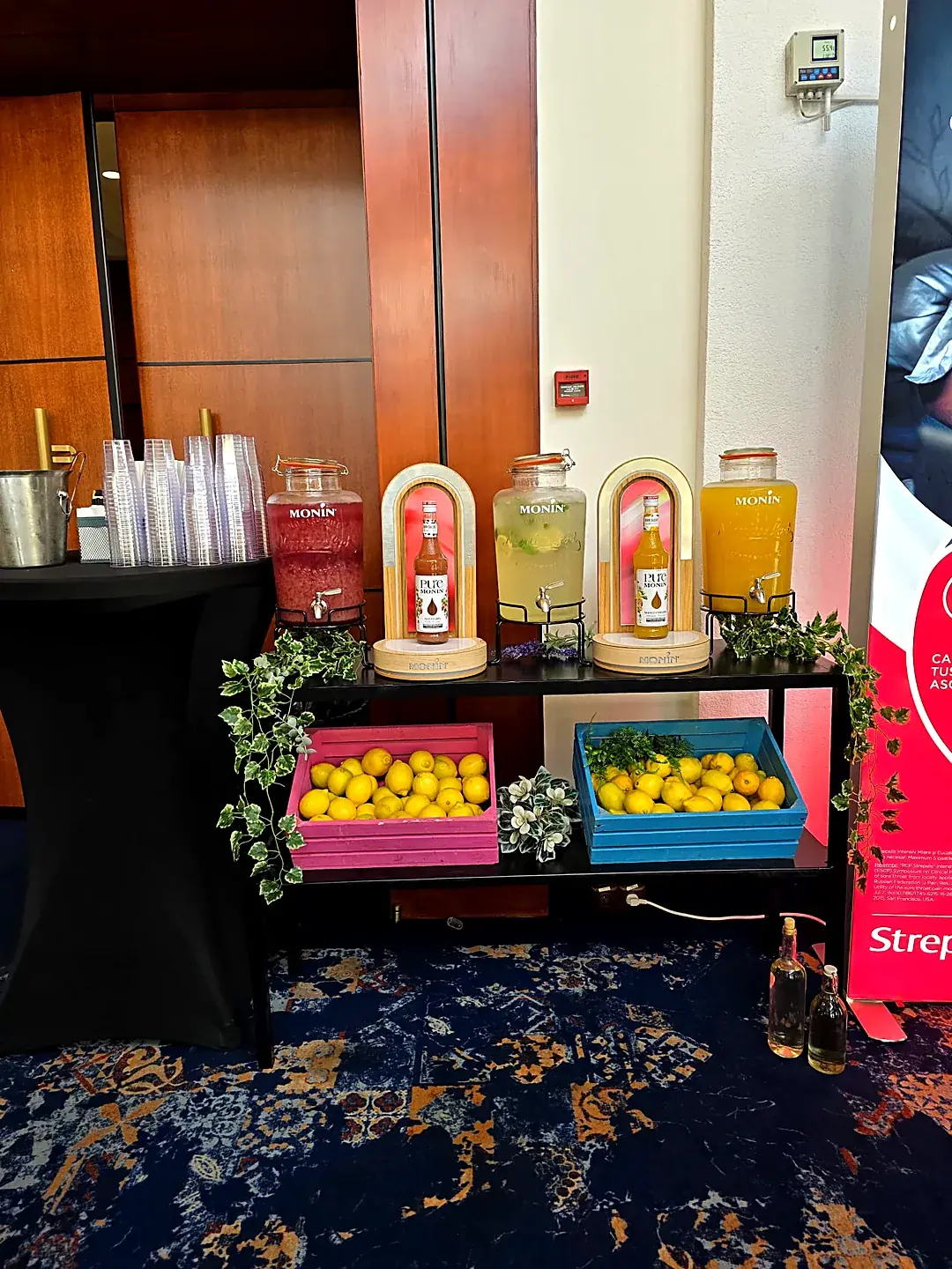 Stație de limonadă artizanală cu dispensere și lădițe cu lămâi, la un eveniment corporate în interior